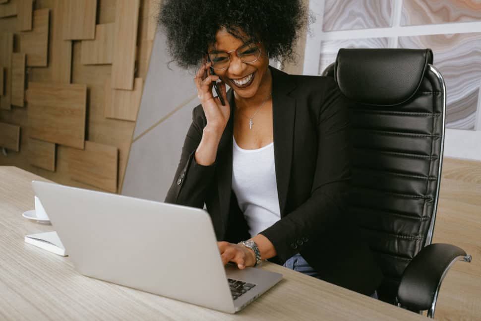 Black woman working on laptop talking on cell phone