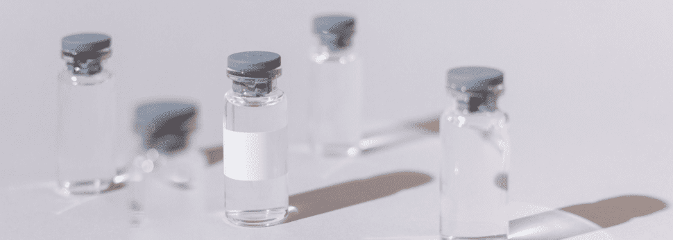 Clear, glass vaccine bottles against a light gray background