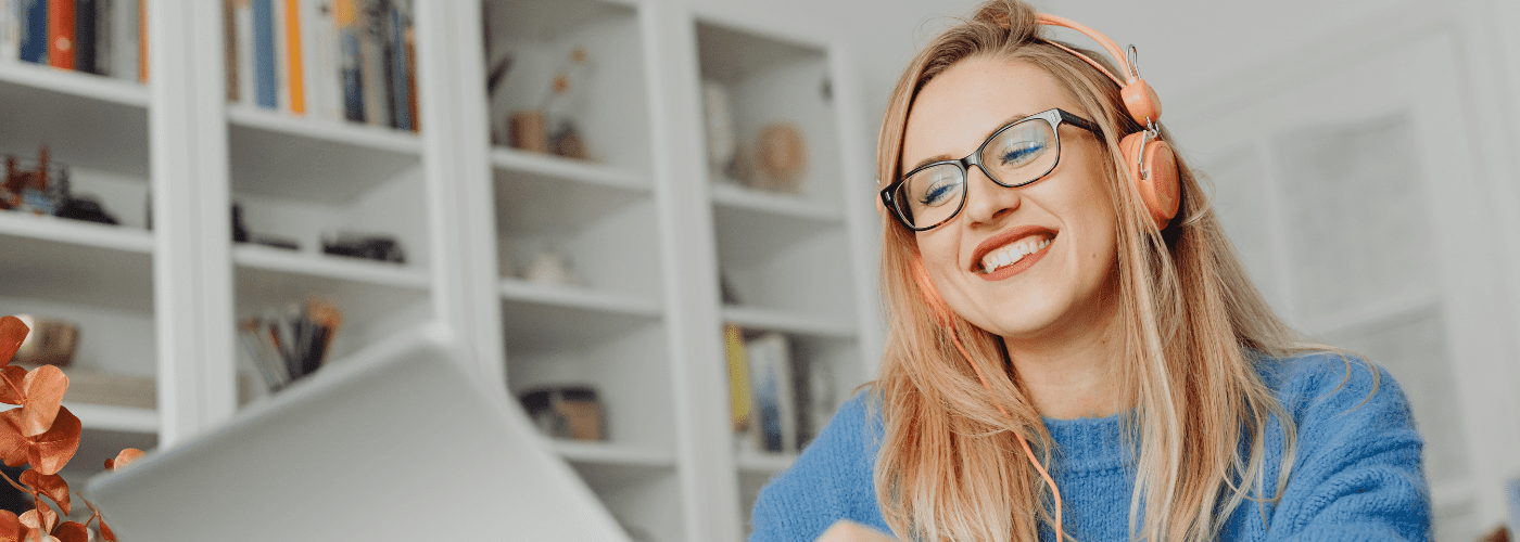 A white woman with blonde hair and glasses smiling at her open laptop due to a positive candidate engagement experience.