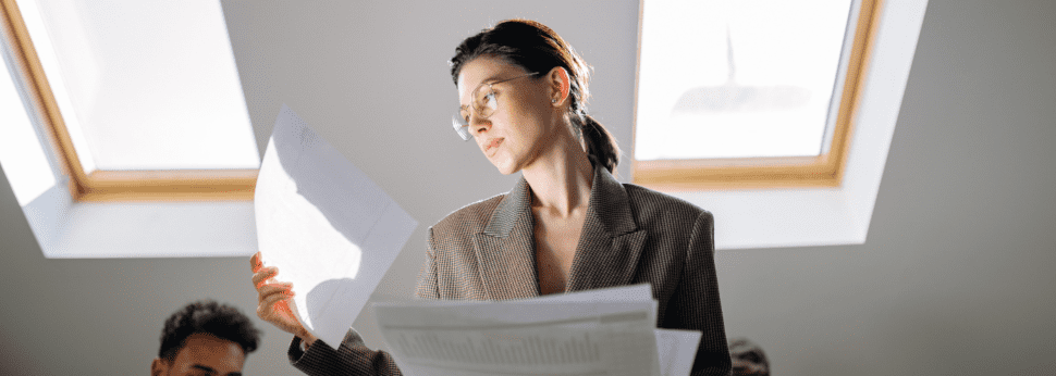 Woman in a light brown suit looks at paper documents for an employee personnel file.